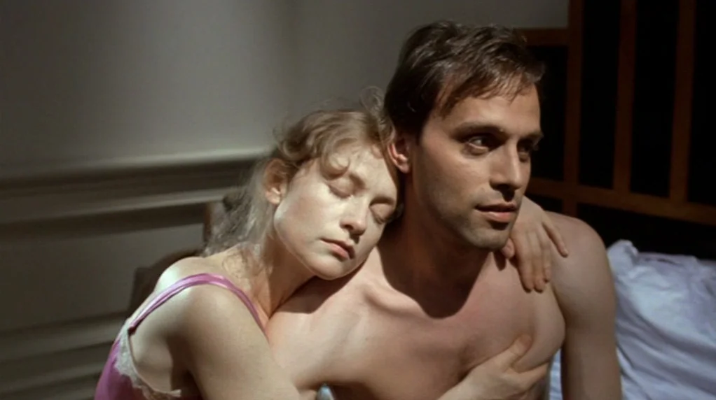 Malina (1991) movie still: medium — A man and woman are lying together in a dimly lit bedroom setting. The woman rests her head against the…