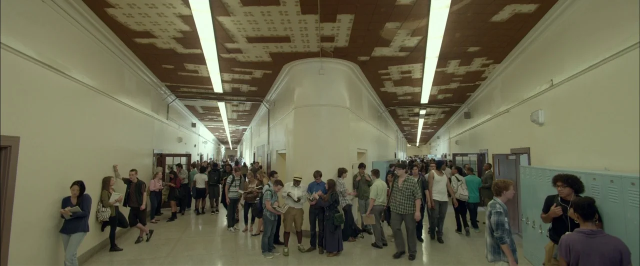 Me and Earl and the Dying Girl (2015) movie still: wide — A long school corridor features cream-colored walls and a brown tiled ceiling with missing…