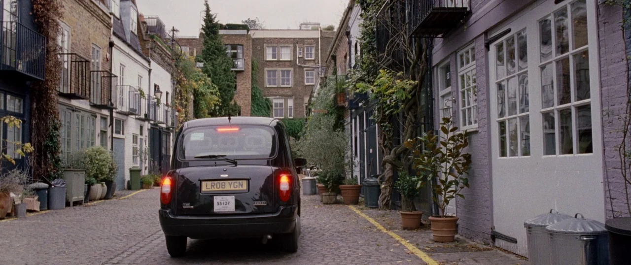 Personal Shopper (2016) movie still: wide — A narrow cobblestone lane features residential brick buildings with iron balconies and potted plants. A…