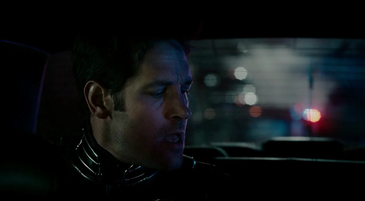 Ant-Man (2015) movie still: closeup — The interior of a moving vehicle at night with blurred city lights visible outside. A man looks toward the…