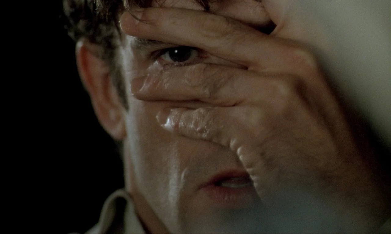 Dellamorte Dellamore (1994) movie still: closeup — A close view shows a man partially covering his face with his own hand. The background is…