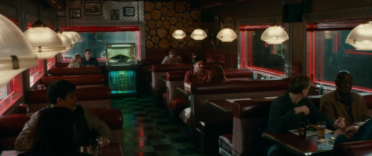 Horns (2013) movie still: wide — A dimly lit diner with red vinyl booths and a black and white checkerboard floor. Several patrons sit in separate…