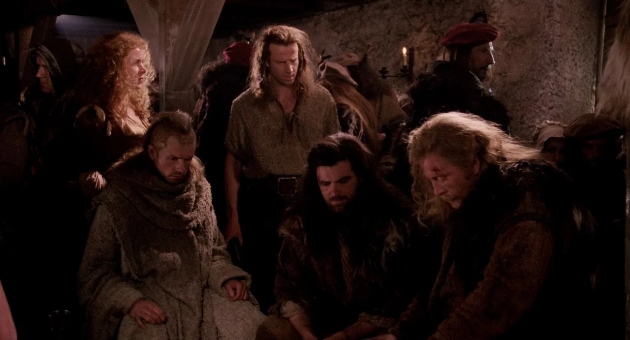 Highlander (1986) movie still: medium — A stone-walled interior space with people gathered in groups under low candle lighting. Several individuals…
