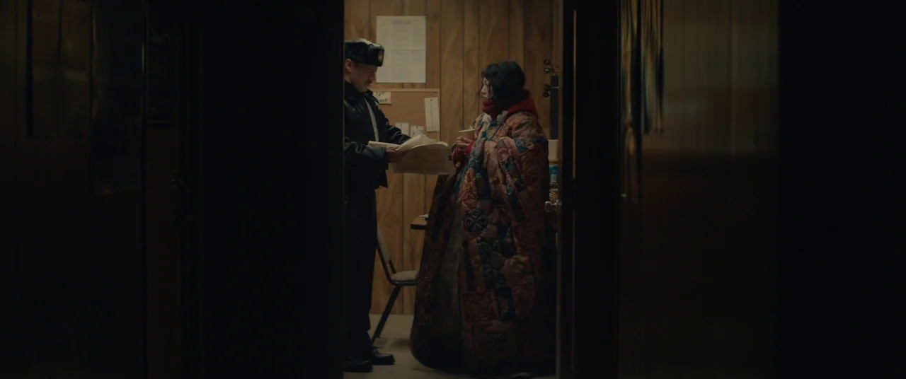 Kumiko the Treasure Hunter (2014) movie still: medium — A dimly lit room with wood-paneled walls and a cork board on the wall. A police officer…