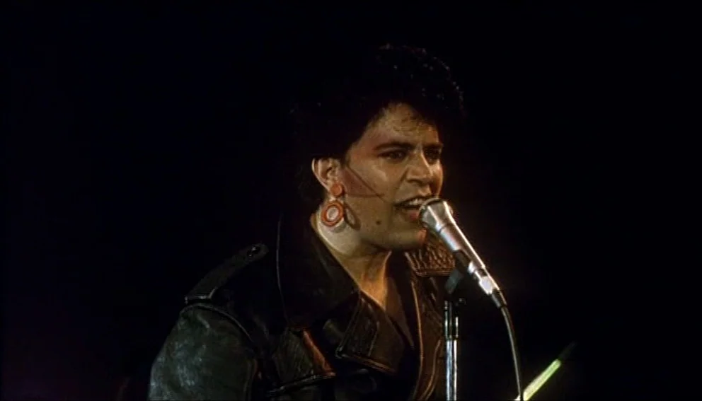 Labyrinth of Passion (1982) movie still: closeup — A dark concert venue with the subject illuminated against a completely black background. A man…