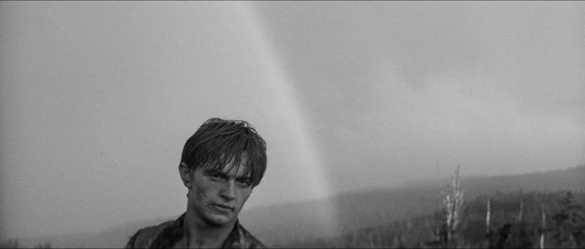 Marketa Lazarová (1967) movie still: medium — A vast, desolate landscape under a cloudy sky shows a faint rainbow. A young man stands in the…