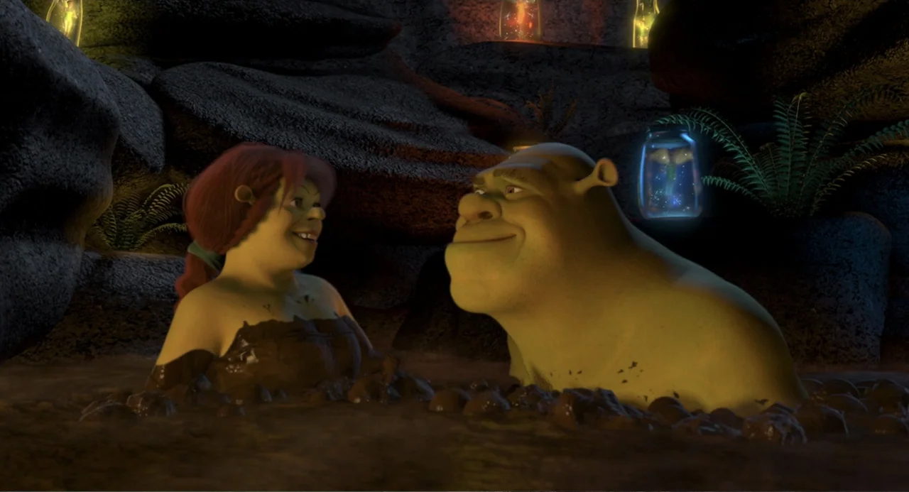 Shrek 2 (2004) movie still: medium — A dark outdoor area filled with mud and surrounded by rough natural rock formations. Two green ogres sit in the…