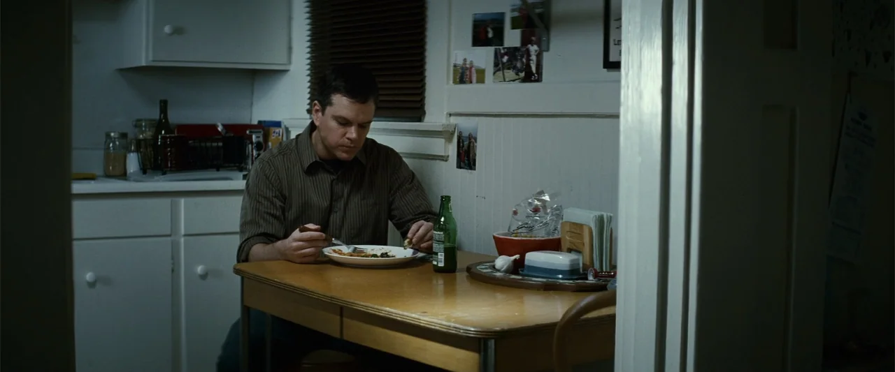 Hereafter (2010) movie still: medium — A dimly lit kitchen dining area features white cabinets and family photographs on the wall. A man in a brown…