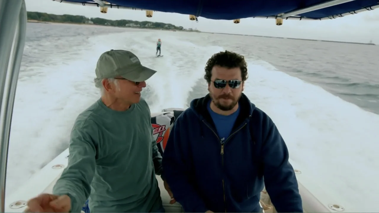 Clear History (2013) movie still: medium — A motorboat cockpit in motion with the ocean visible in the background. Two men are operating the boat…