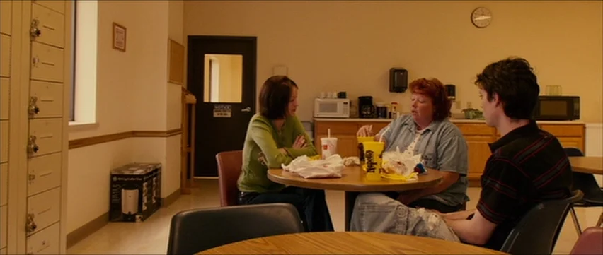 Bubble (2005) movie still: wide — A sparse, beige-walled break room contains metal lockers, a small table, and microwave appliances. Three people…