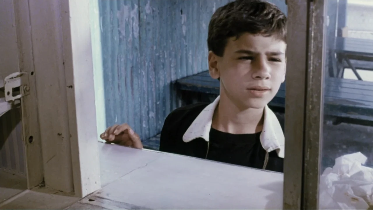 Aunt Mary (1979) movie still: medium — A small interior booth with a white counter and blue textured walls. A young boy leans over the edge of the…