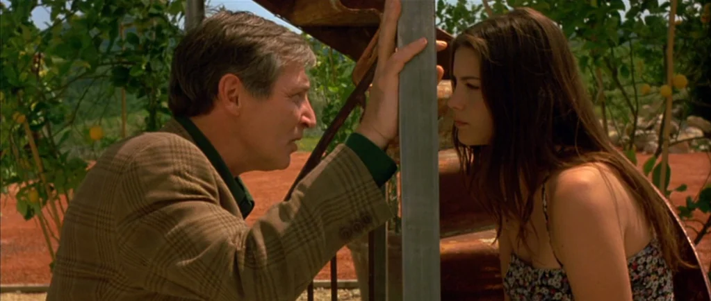 Stealing Beauty (1996) movie still: medium — An outdoor lemon orchard with rows of trees lines the background behind the subjects. An older man and…