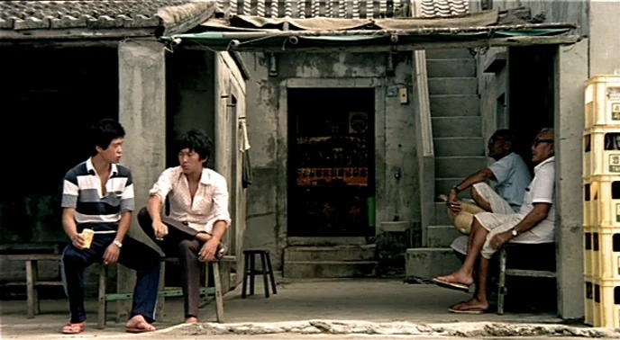 The Boys From Fengkuei (1983) movie still: wide — A weathered concrete courtyard with a simple wooden overhang and a stone staircase entrance. Four…