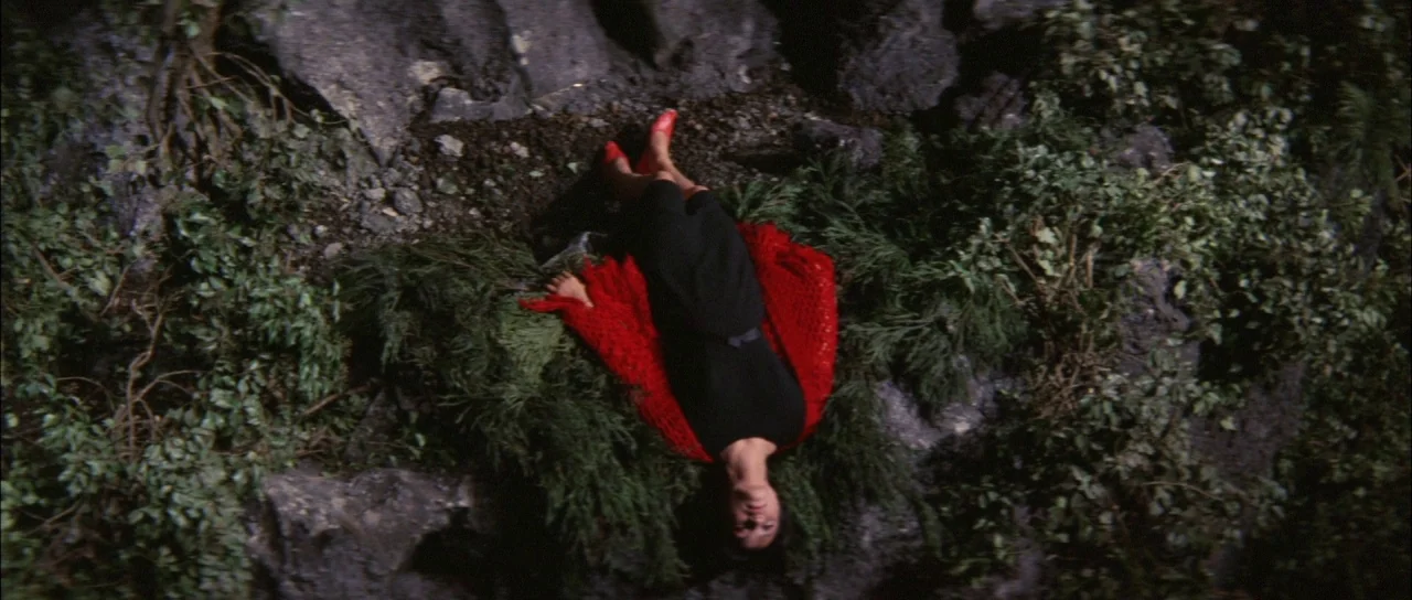 Ghidorah The Three Headed Monster (1964) movie still: fullbody — A woman lies flat on dark, uneven rocks surrounded by patches of low-lying…