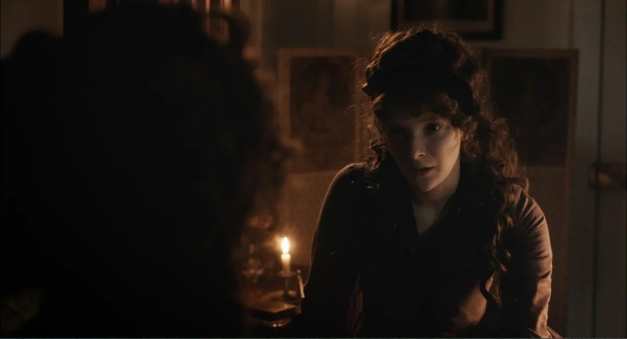 Love & Friendship (2016) movie still: medium — A dimly lit 19th-century bedroom features a wooden folding screen in the background. A woman with…