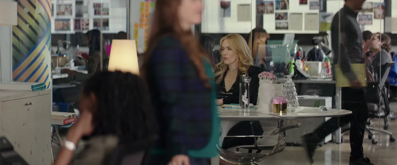 Collateral Beauty (2016) movie still: medium — A busy open plan office features glass partitions and various work desks. A woman sits at her desk…