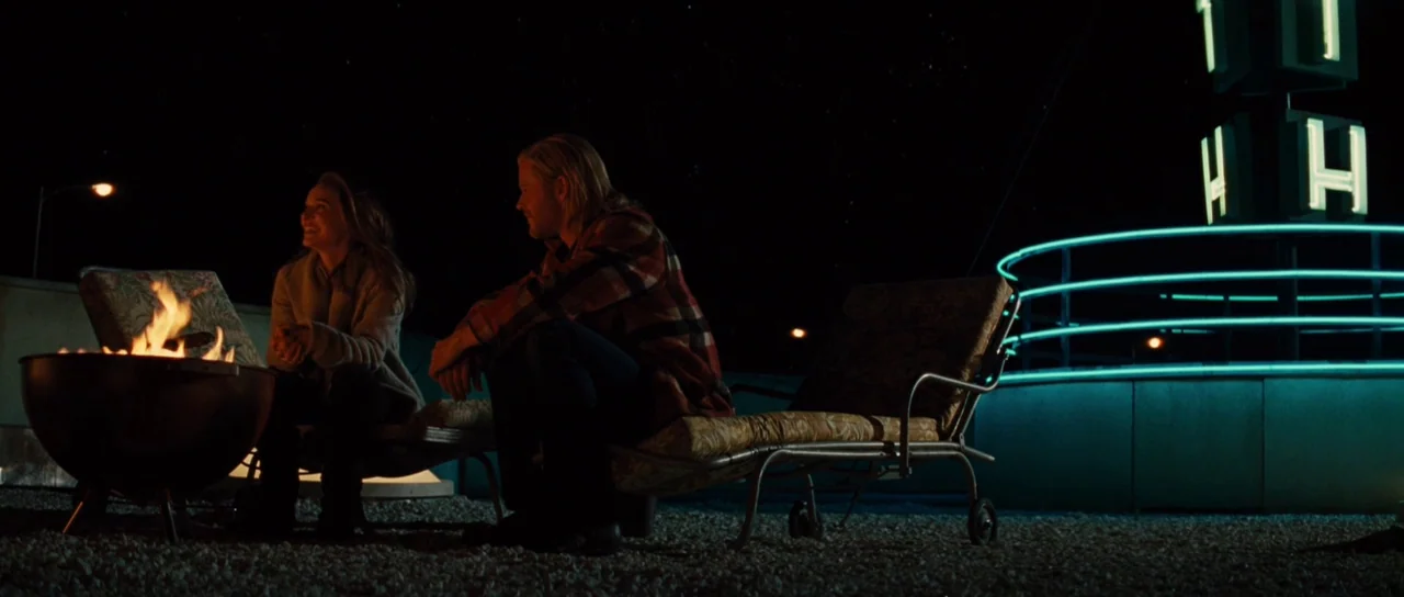 Thor (2011) movie still: wide — A rooftop at night features a gravel surface, lounge chairs, and a metal fire pit. A man and a woman sit facing each…