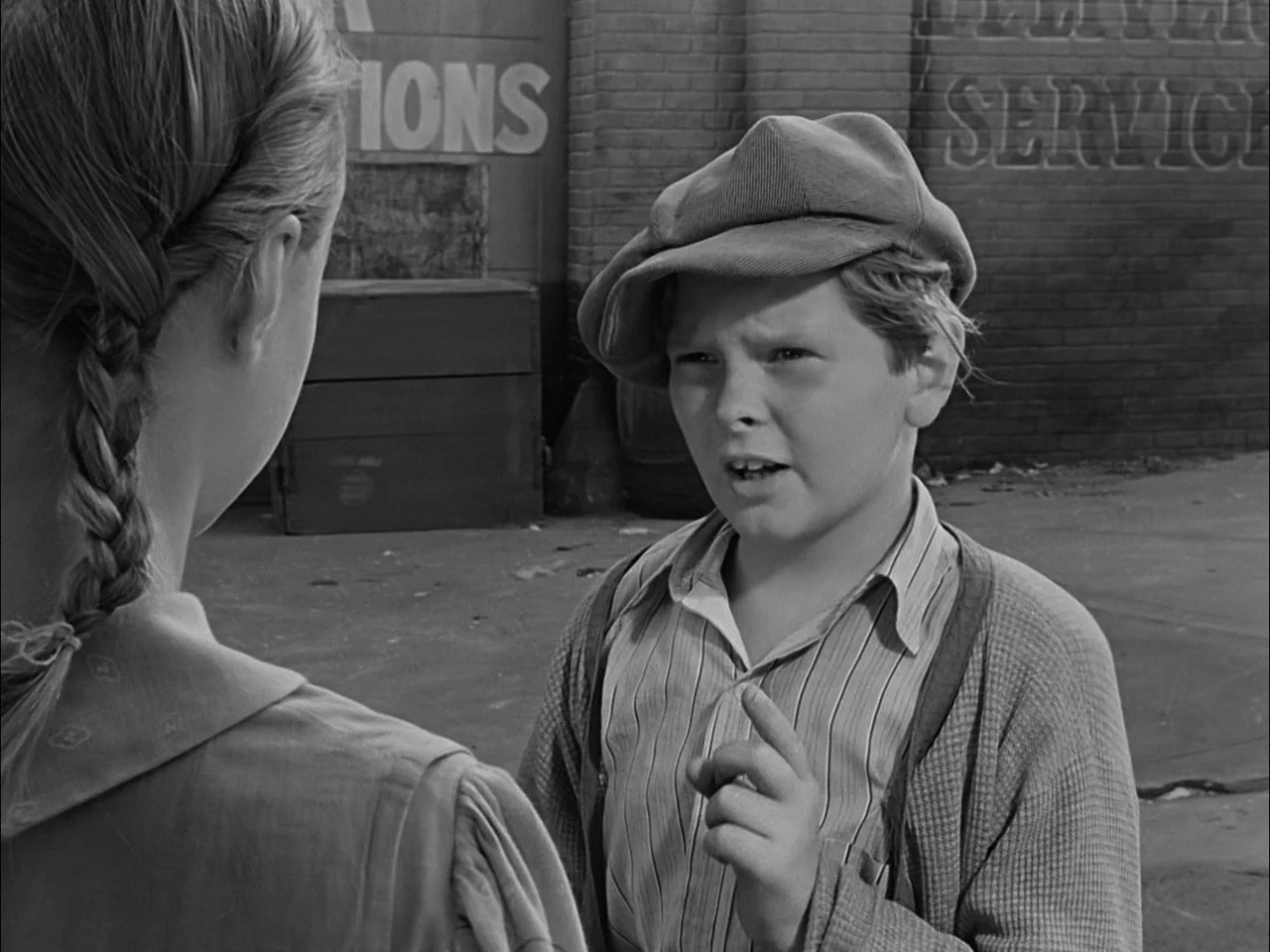 A Tree Grows In Brooklyn (1945) movie still: medium — Two children stand facing each other in front of a brick building exterior. The boy in a cap…