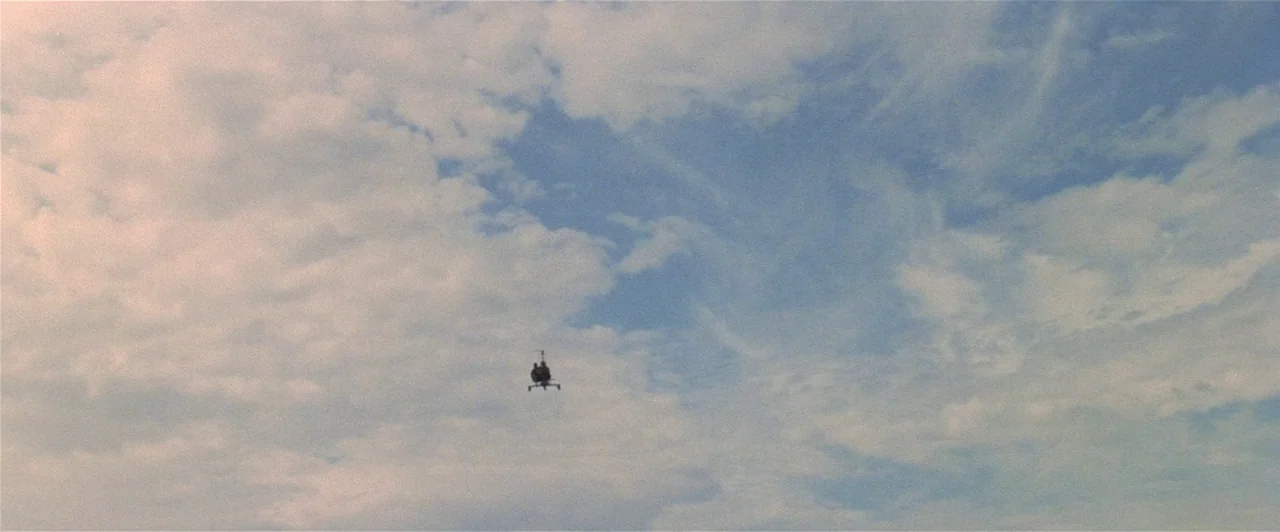 Mad Max 2 (1981) movie still: establishing — A vast sky is filled with white scattered clouds during the daytime. A tiny silhouette of a helicopter…