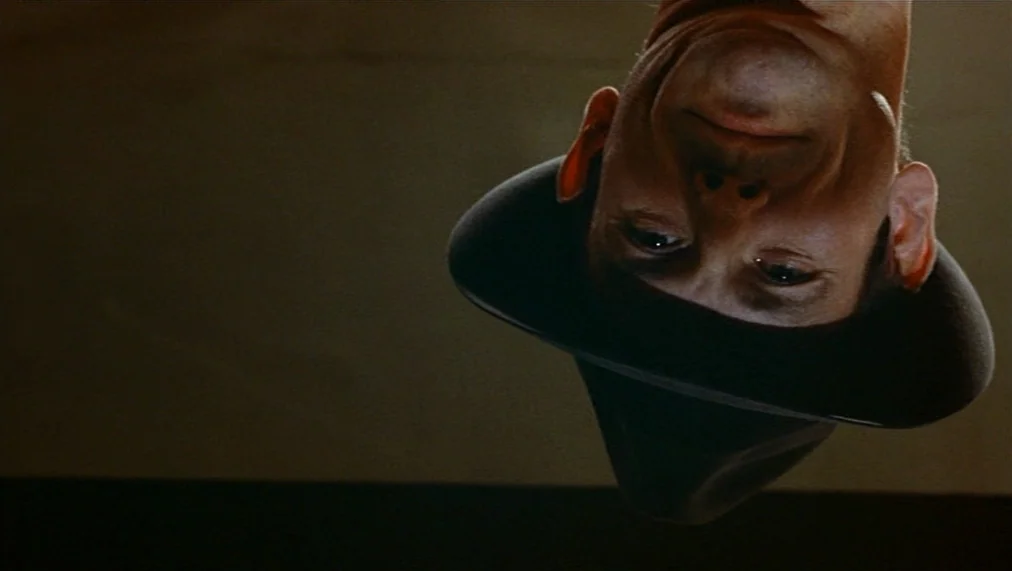 The Marriage of Maria Braun (1979) movie still: closeup — A man wearing a fedora is framed in an extreme low-angle, upside-down perspective. The man…