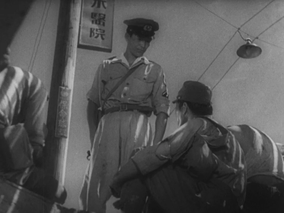 Stray Dog (1949) movie still: medium — A dark, dimly lit urban street corner with a utility pole and signage. A standing police officer observes a…