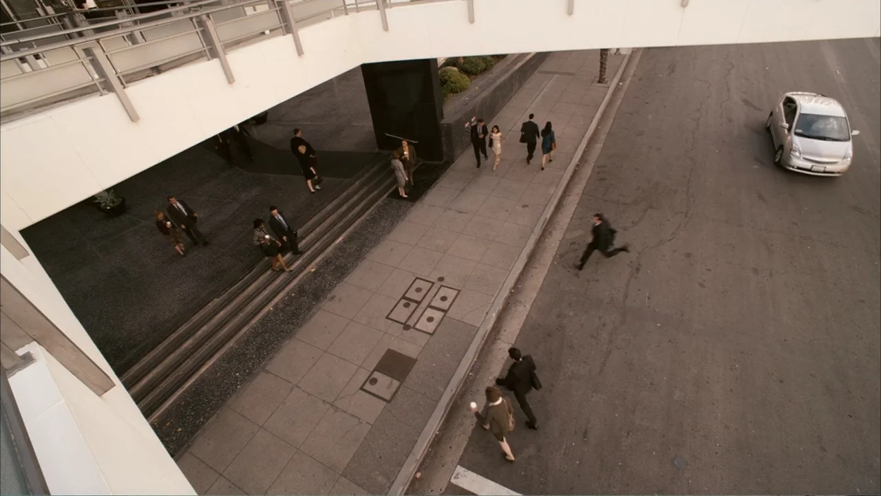Get Smart (2008) movie still: wide — A modern concrete plaza features a pedestrian walkway adjacent to a city road. Several professionals in…