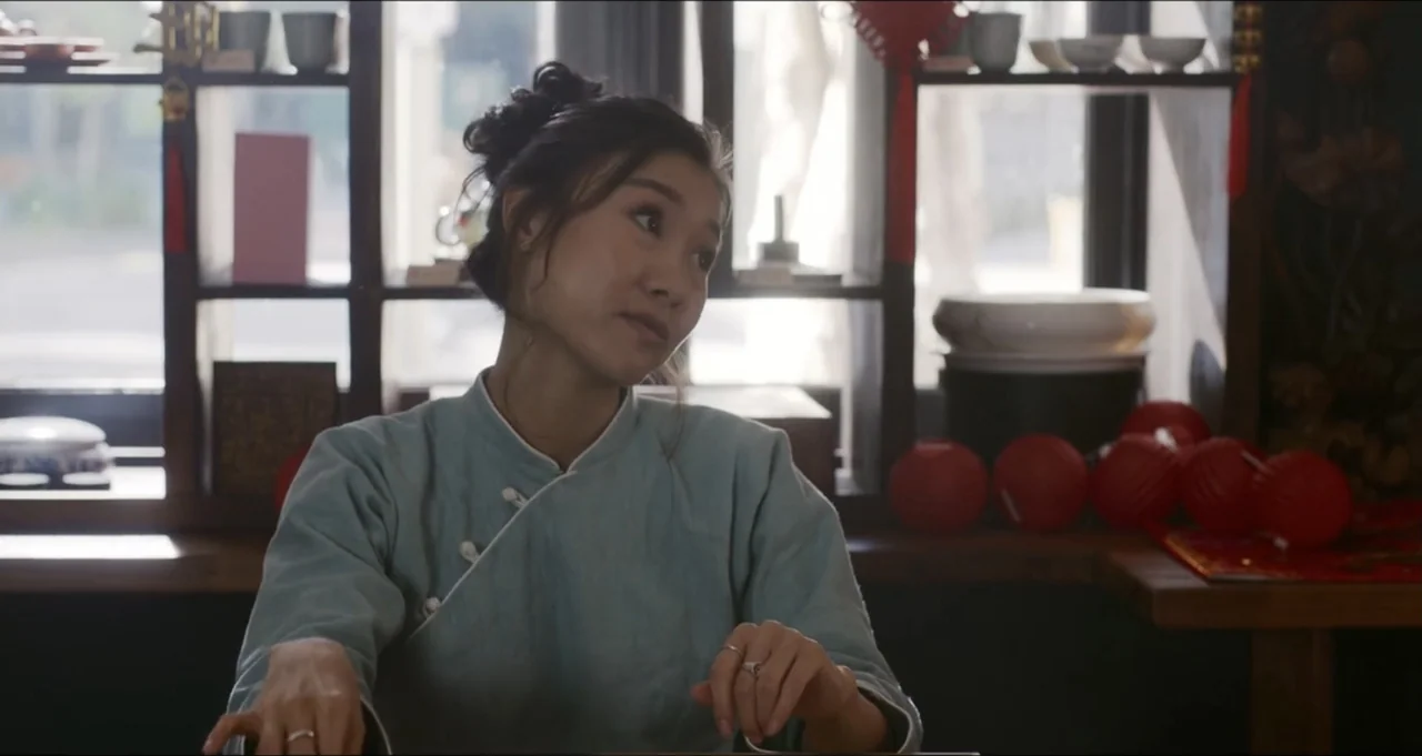 Five Blind Dates (2024) movie still: medium — A room with wooden shelving displaying ceramics and small red paper lanterns on counters. An East…