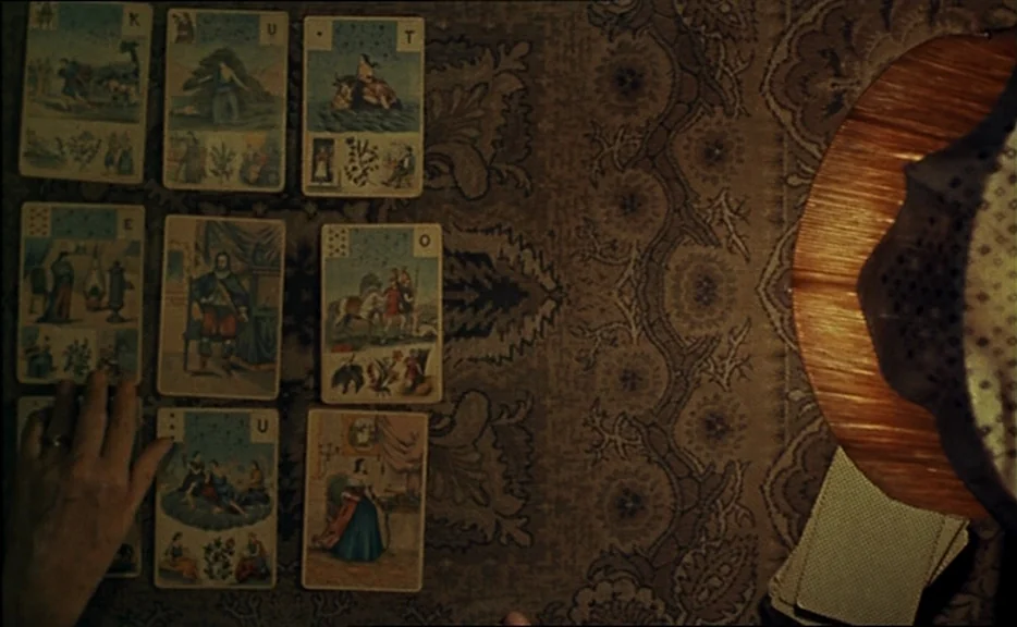 Cléo from 5 to 7 movie still: closeup — Vintage fortune-telling cards are laid out in a grid pattern on a patterned tablecloth. A person's hand…