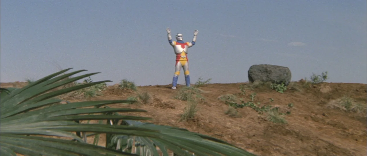 Godzilla Vs Megalon (1973) movie still: wide — A desolate hillside with brown soil and sparse patches of wild, dry grass. A costumed robot figure…