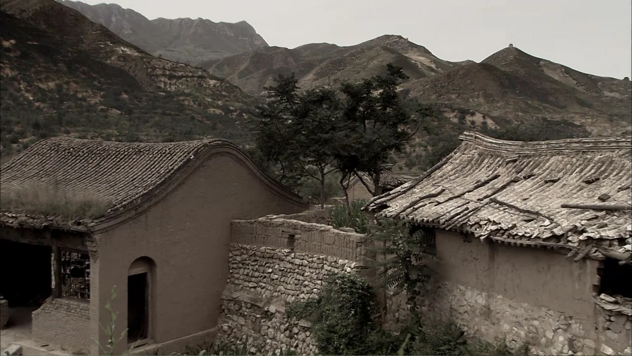 The First Emperor (2006) movie still: establishing — A remote rural village features earthen mud houses with traditional curved tile roofs. Rugged…