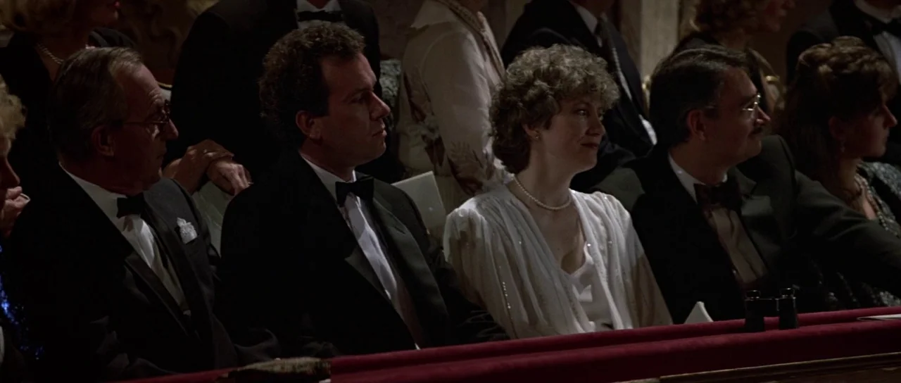 The Living Daylights (1987) movie still: medium — An audience in formal wear sits in the box seats of an old theater. A man and a woman in the…