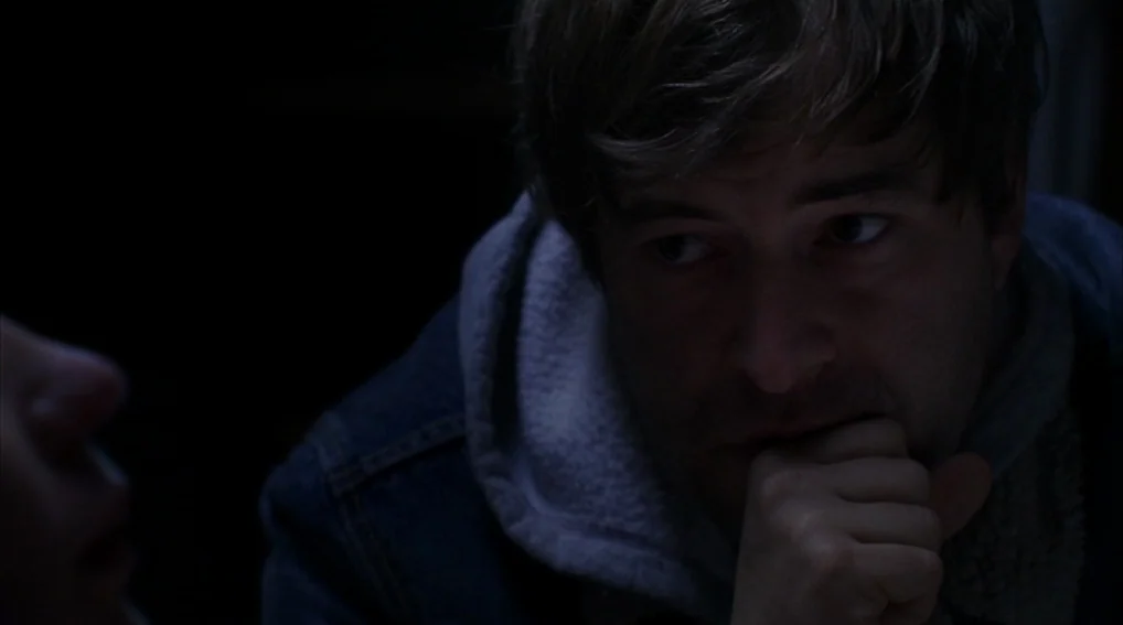Your Sister’s Sister (2011) movie still: closeup — A dark, dimly lit interior setting obscures most architectural details. A man with messy hair…