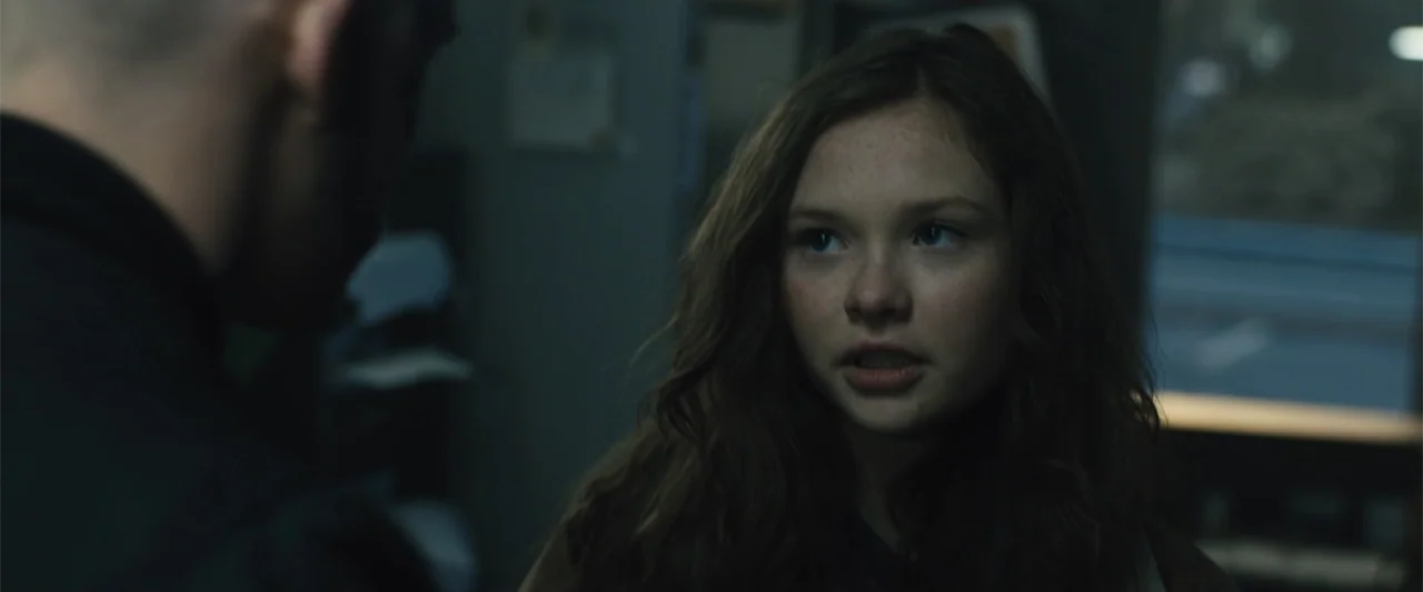 Skin (2009) movie still: medium — An interior space contains a young woman and an out-of-focus individual in the foreground. The girl turns her head…