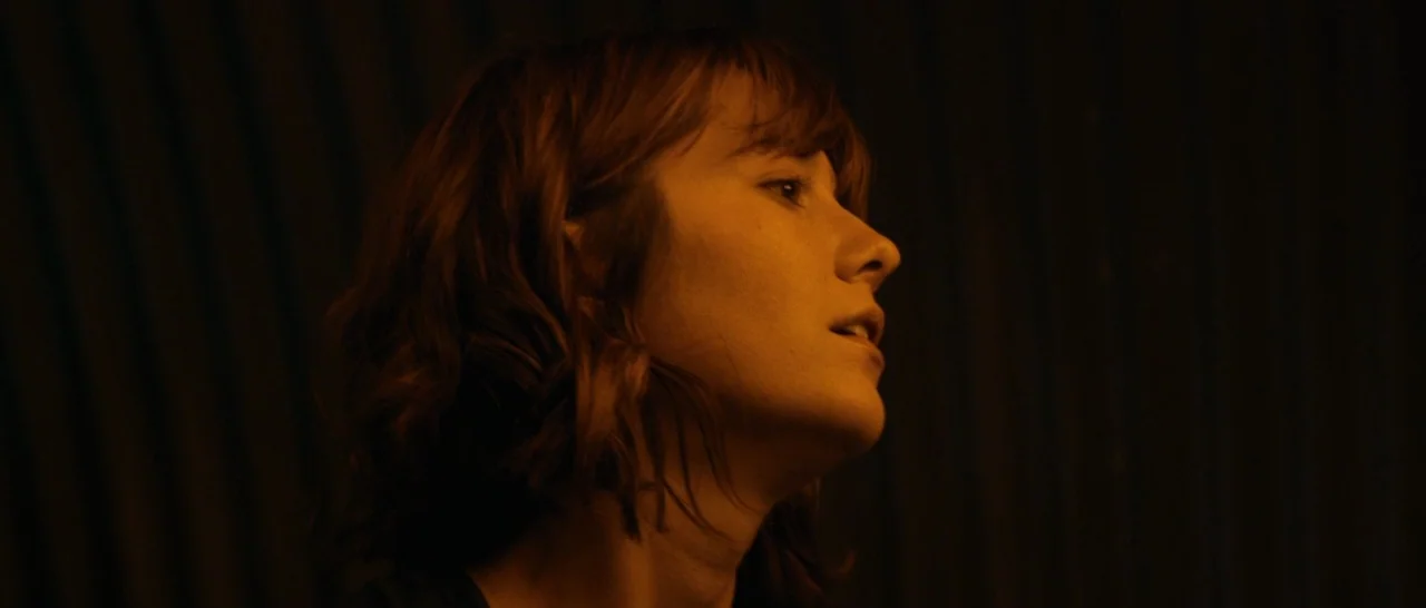 10 Cloverfield Lane (2016) movie still: closeup — The subject stands in a dimly lit, dark-toned interior space with corrugated wall texture. The…
