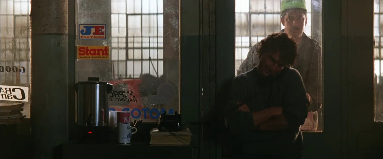 Days of Thunder (1990) movie still: medium — An auto repair shop interior features a glass-partitioned office with automotive supply stickers…