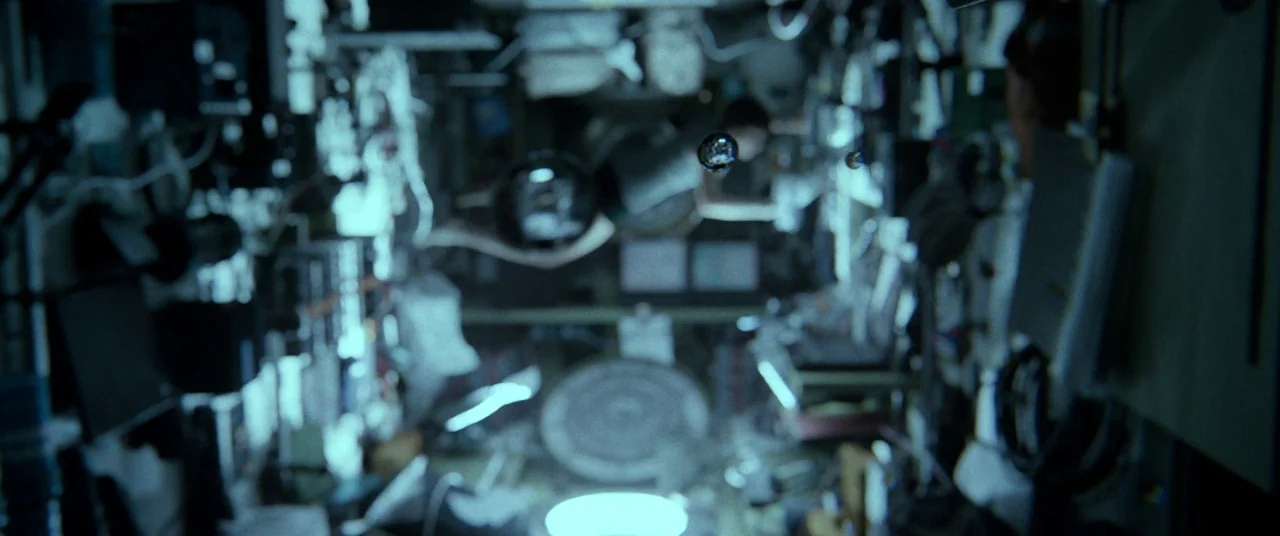 Gravity (2013) movie still: wide — The interior of a cramped space station is filled with technical equipment and wiring. Water droplets drift in…