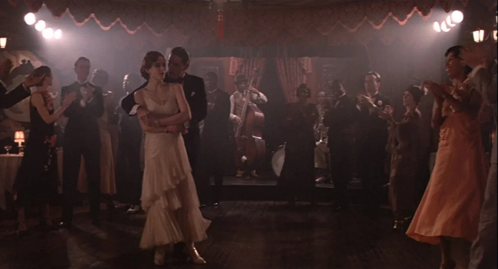 The Cotton Club (1984) movie still: fullbody — A dimly lit 1920s jazz ballroom features a dance floor filled with people. A couple dances in the…