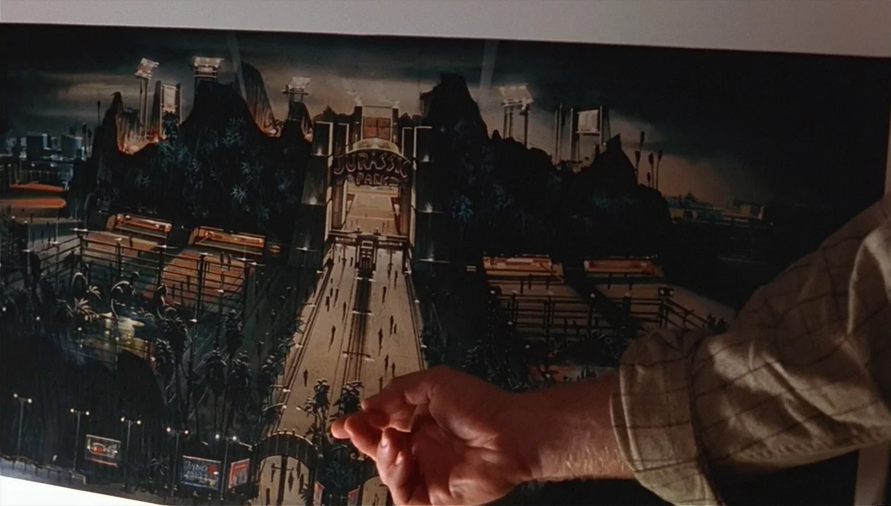 The Lost World: Jurassic Park (1997) movie still: medium — A man's hand points toward a framed conceptual drawing of a themed amusement park. The…