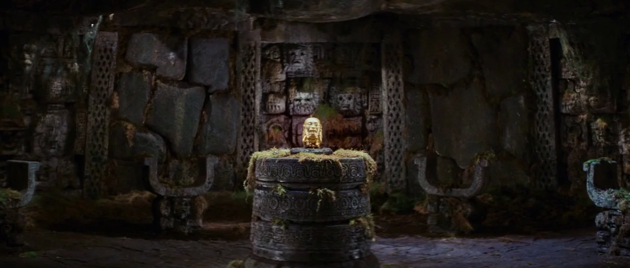 Raiders Of The Lost Ark (1981) movie still: wide — A stone chamber features carved walls with moss-covered surfaces and U-shaped stone seats. A…