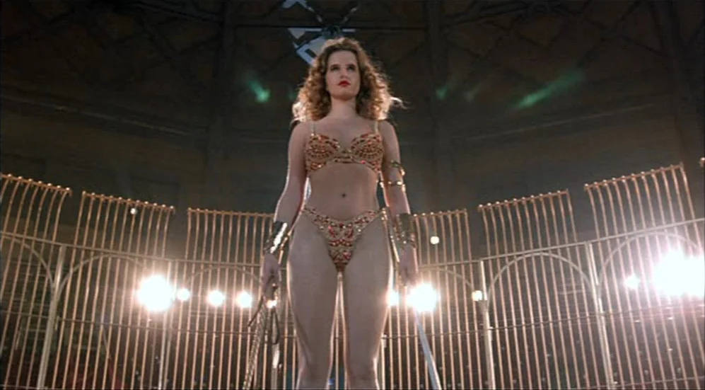 Roselyne and the Lions (1989) movie still: fullbody — A woman stands in the center of a circular metal-fenced performance arena. Bright stage lights…