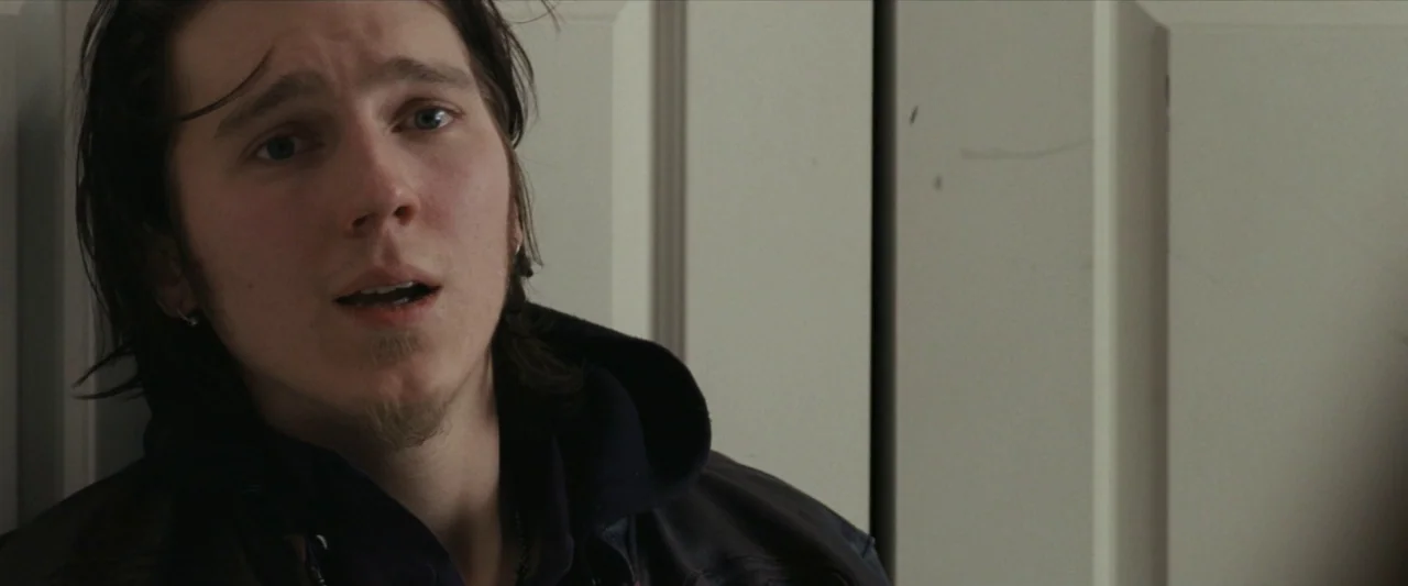 For Ellen (2012) movie still: closeup — A man stands before a closed white door with vertical paneling. The subject looks off-camera with his mouth…