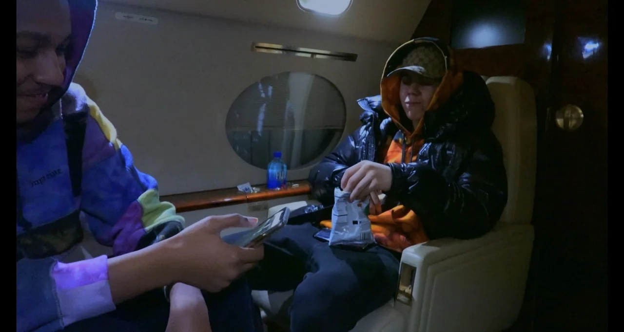 Juice WRLD: Into the Abyss (2021) movie still: medium — A private jet cabin features oval windows and plush light-colored leather seating. Two young…
