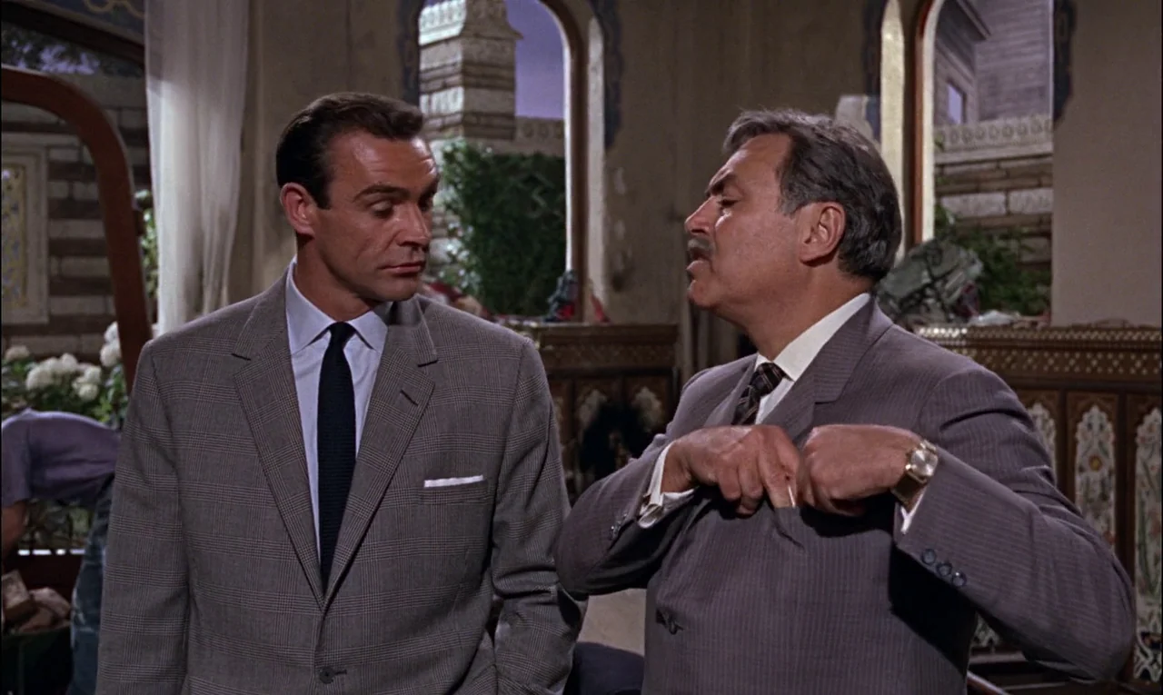 From Russia With Love (1963) movie still: medium — An interior space features arched windows overlooking an outdoor area with greenery. A man in a…