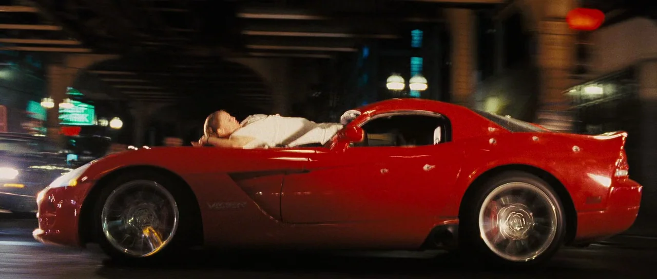 Wanted (2008) movie still: wide — A bright red sports car drives beneath urban overpasses at high speed during night. A woman lies flat on the car's…