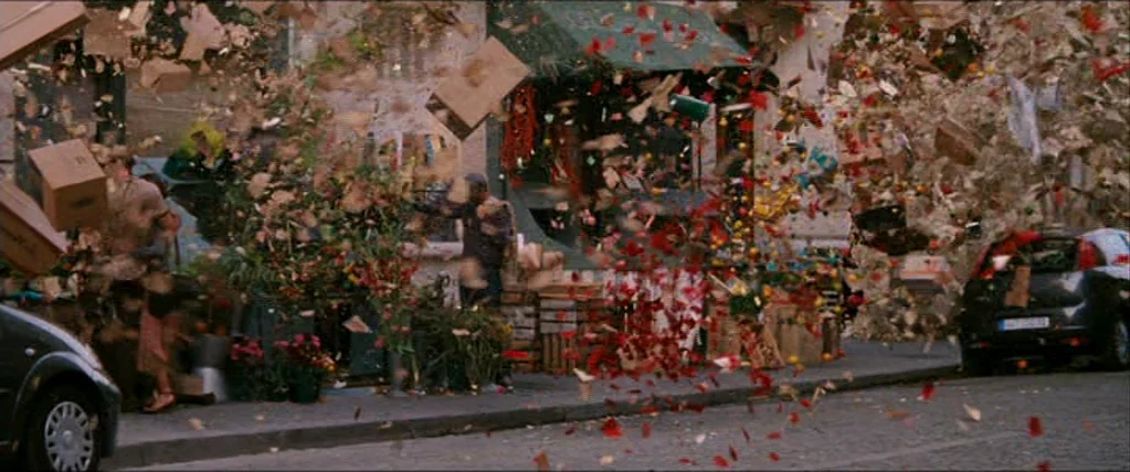 Inception (2010) movie still: wide — A city street front is cluttered with floating cardboard boxes and scattered floral debris. The air is thick…