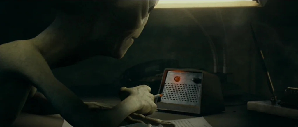 Paul (2011) movie still: closeup — A dimly lit desk with a vintage intercom or radio unit sits in shadows. An extraterrestrial creature with slender…