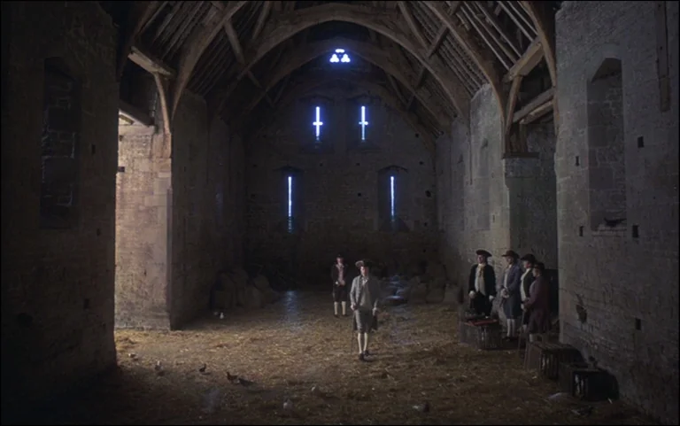 Barry Lyndon (1975) movie still: wide — A spacious stone barn features exposed wooden roof beams and narrow slit windows. A small group of men in…