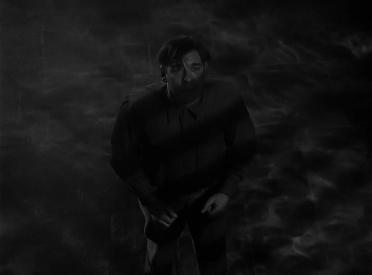 The Wolf Man (1941) movie still: medium — A man stands on a dark wet surface at night with fog swirling around him. The scene is lit by harsh light…
