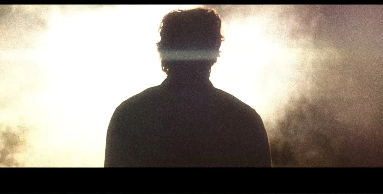 Alien Abduction: Travis Walton (2022) movie still: medium — An outdoor field at sunset with hazy light conditions and blurred vegetation. A lone man…