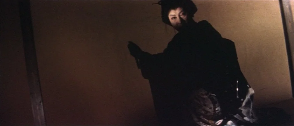 An Actor’s Revenge (1963) movie still: medium — A dimly lit room with plain walls features a figure in traditional attire. The person kneels on the…